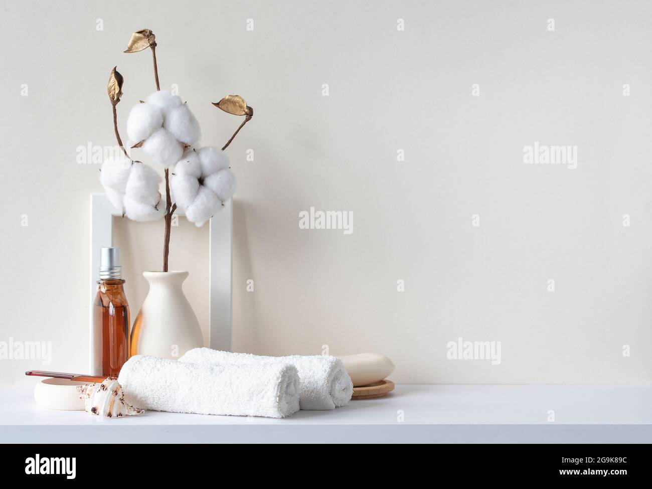 Gli interni del bagno sono in tonalità pastello beige. Ripiano bianco in bagno con asciugamani, sapone, bottiglia di profumo, spazzola per capelli, piante di casa. Mockup con spazio per il testo. Foto Stock