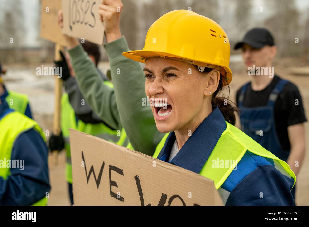 Molto arrabbiato donna costruttore e i suoi colleghi con cartelli che gridano sullo sciopero Foto Stock