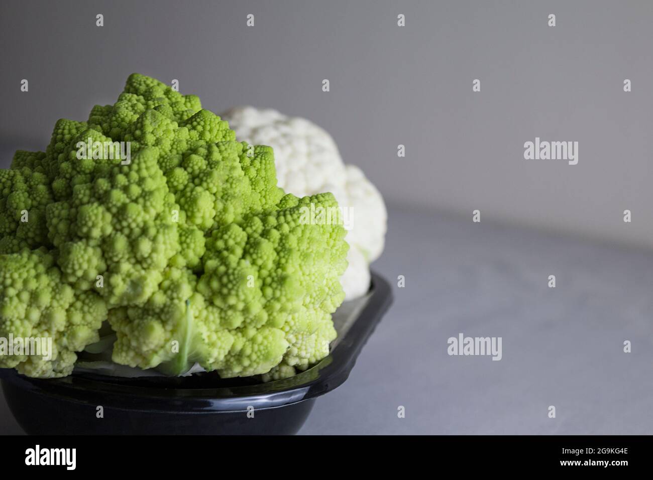 cavolfiore e cavolfiore romanesco su un piatto nero. Sfondo grigio Foto Stock