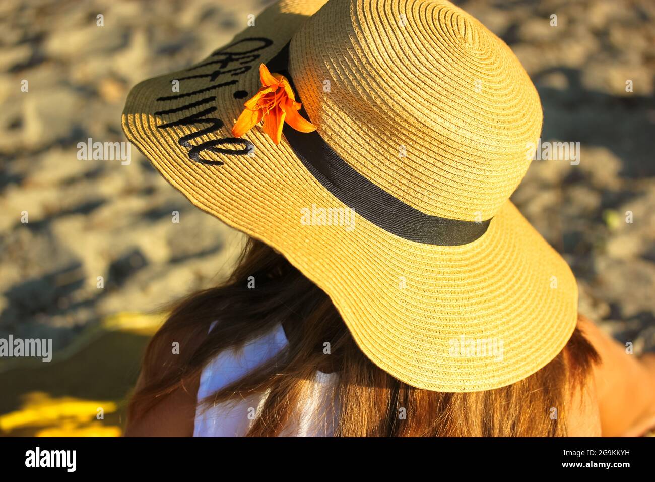 Una ragazza in un cappello di paglia con una parola scritta Offline su di  esso, adornata con un giglio arancione sta riposando sul mare in una  giornata estiva soleggiata. Vista dal b