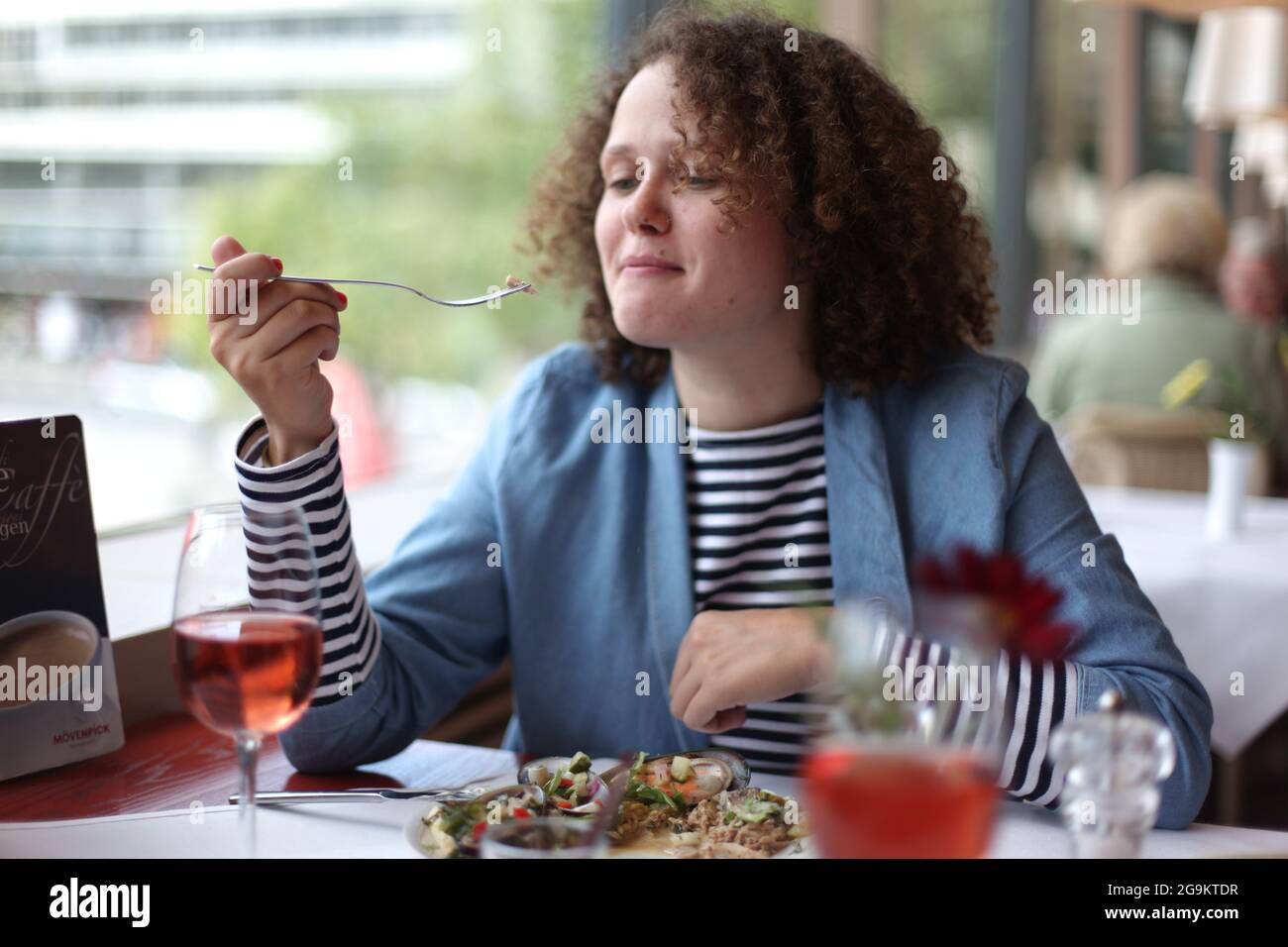 Donna felice con capelli ricci che indossa abiti casual mangiare yummy insalata fresca mentre si pranza in ristorante Foto Stock