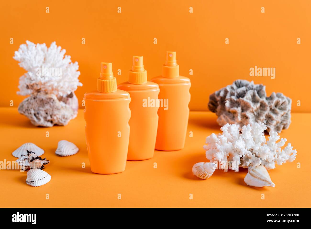 coralli e bottiglie di mare con crema solare su sfondo arancione Foto Stock