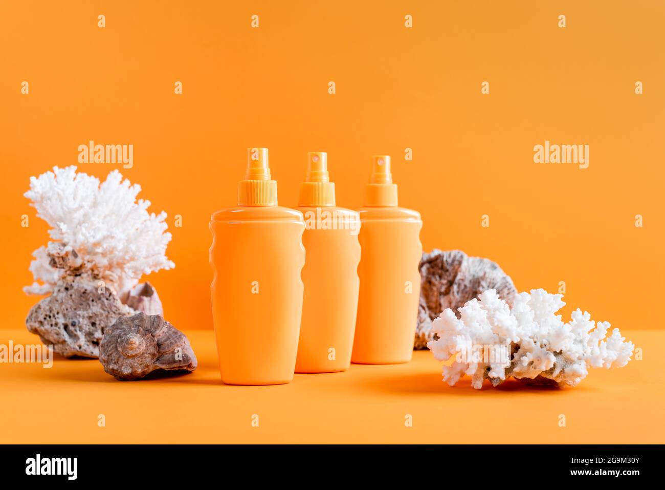 spruzzare bottiglie di crema solare vicino ai coralli marini isolati su arancione Foto Stock