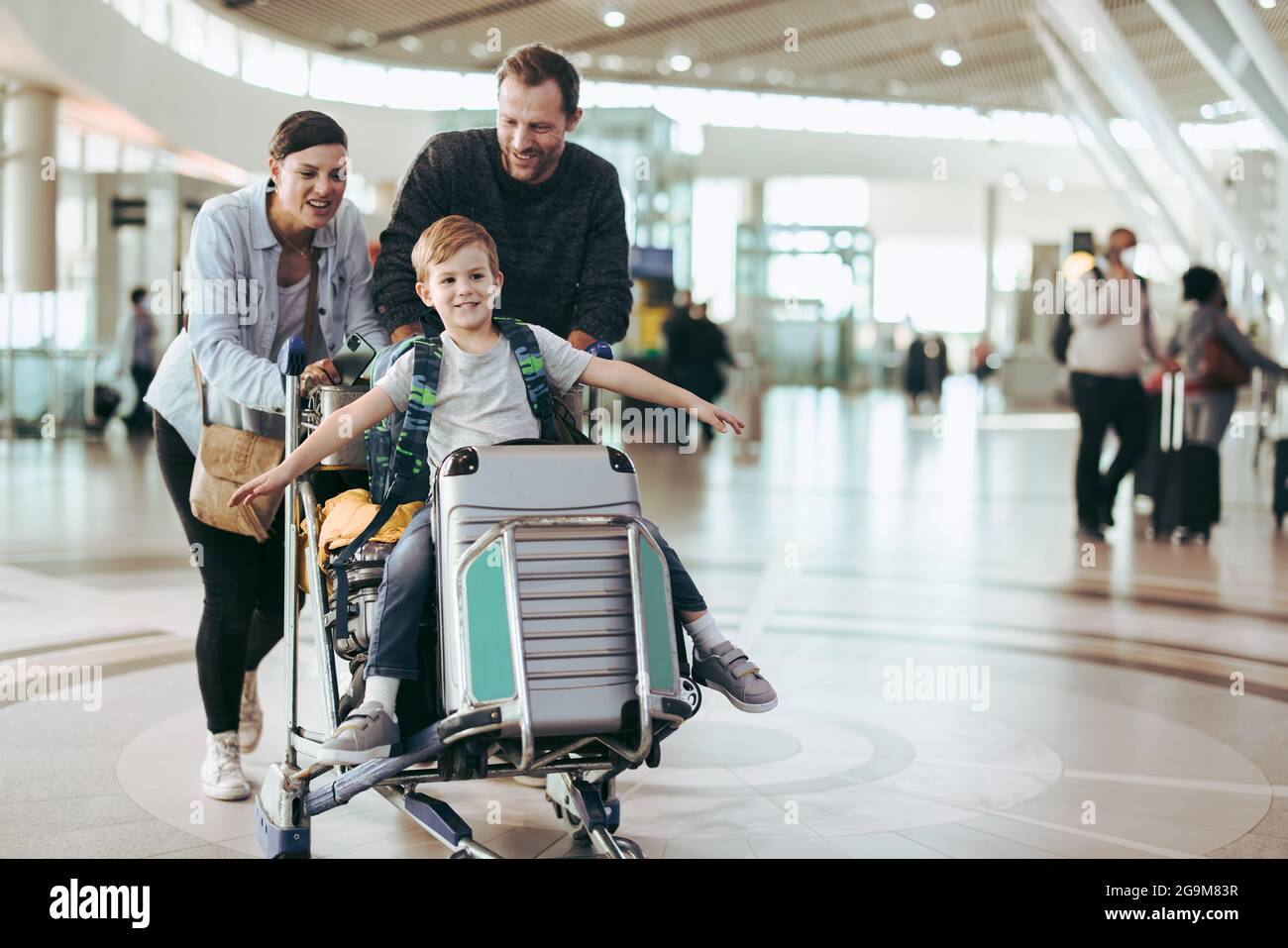 I genitori spostano il carrello dei bagagli con il figlio all'aeroporto. Coppia che spinge il trolley con il figlio all'aeroporto. Foto Stock
