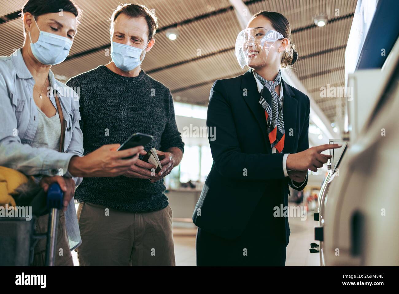 Il personale dell'aeroporto con una coppia che aiuta a compilare i dettagli della macchina self-service durante la pandemia. Coppia turistica in maschere di faccia a self-service aiutato da un Foto Stock