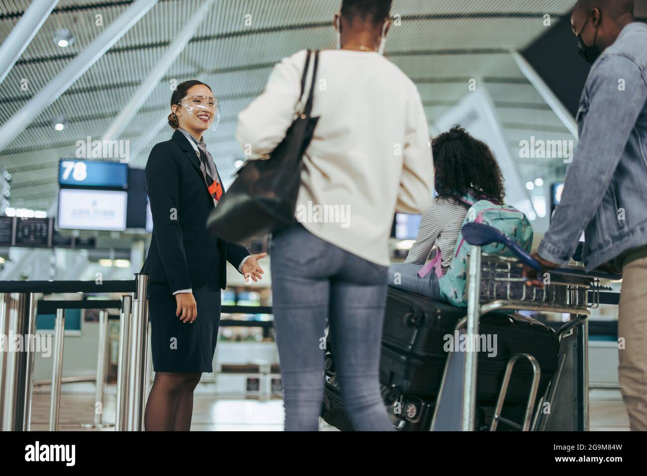 Il personale dell'aeroporto durante la pandemia aiuta la famiglia al cancello d'imbarco. Il personale di terra all'aeroporto assiste il turista in maschere di faccia durante la pandemia. Foto Stock