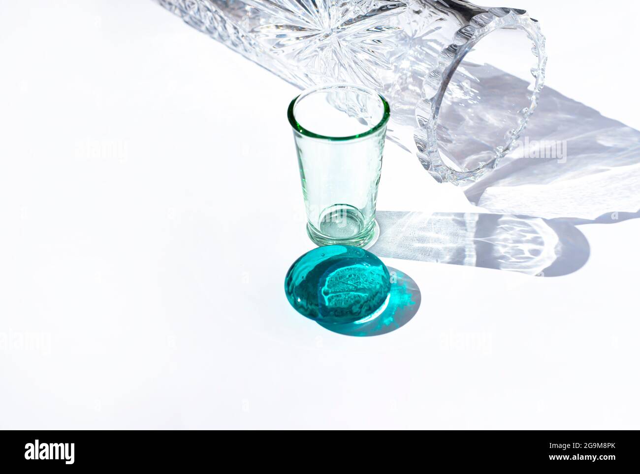 Recipienti di vetro di varie forme e colori. Ombre e riflessi. Vaso. Bicchiere di tequila. Cerchio di vetro turchese. Foto Stock