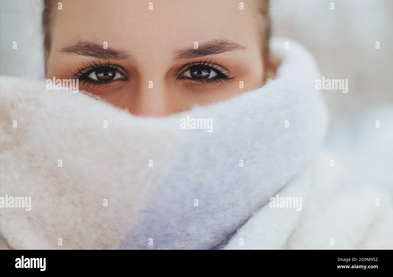 Closeup foto di bella bruna femmina con un look affilato, metà della giovane donna viso coperto di colore chiaro sciarpa lavorato a maglia, ragazza che guarda in camer Foto Stock