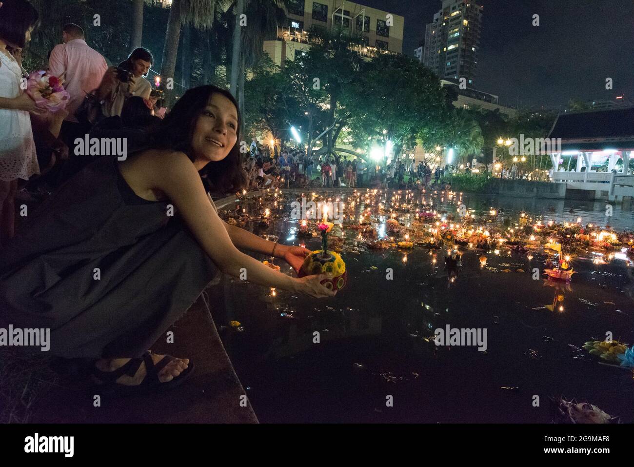 Una giovane donna tailandese lancia un krathong sullo stagno del parco di Benjasiri, a Bangkok, in Thailandia. Foto Stock