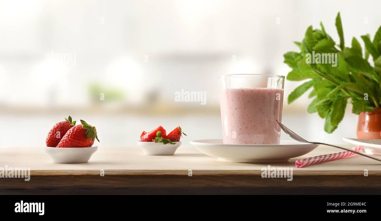 Bicchiere pieno di frullato di fragola su panca di legno piena di frutta in cucina. Vista frontale. Foto Stock