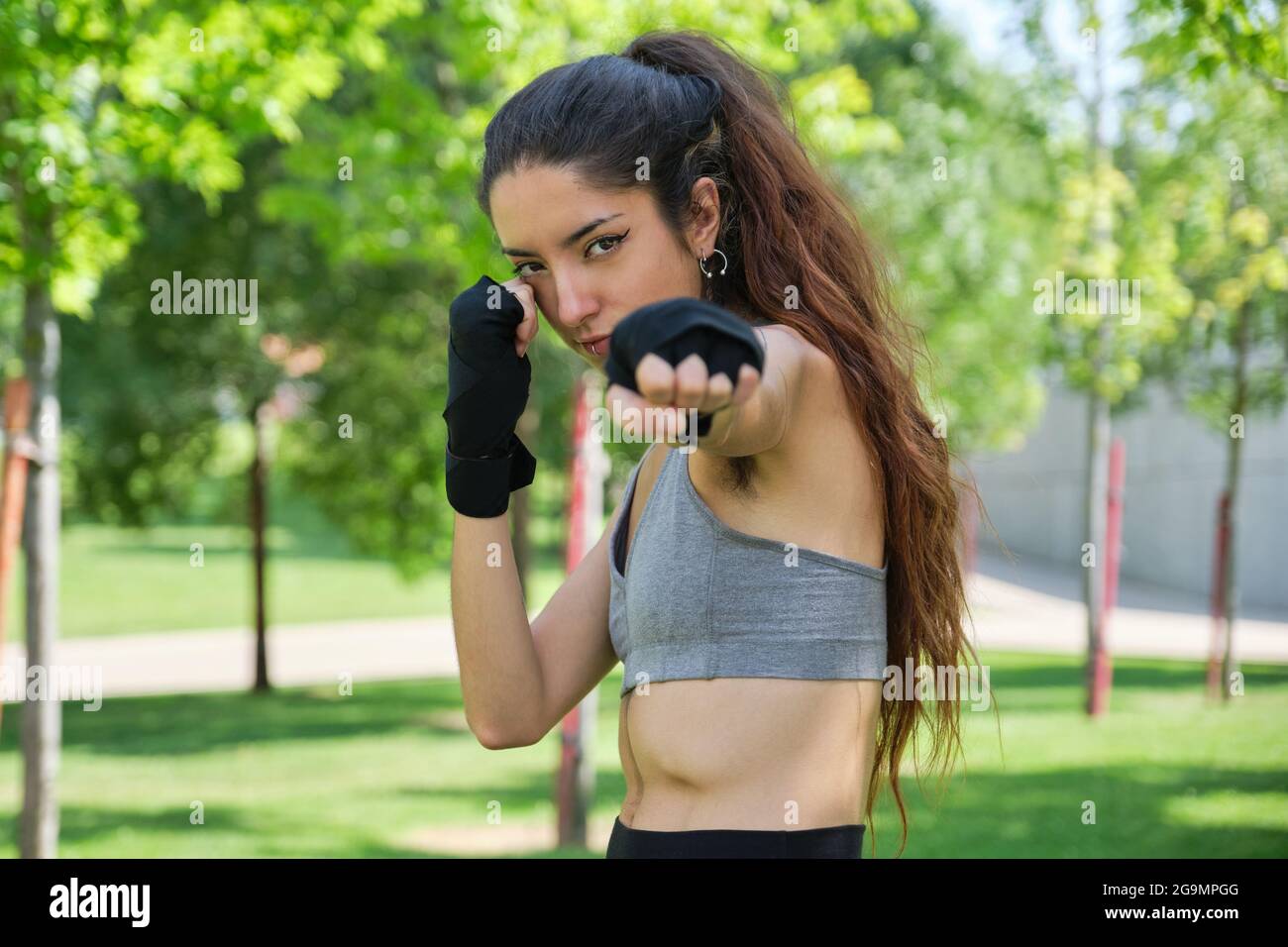 Nessuna persona binaria in mano si avvolge colpendo e guardando la telecamera. Muay thai, sport all'aperto. Foto Stock