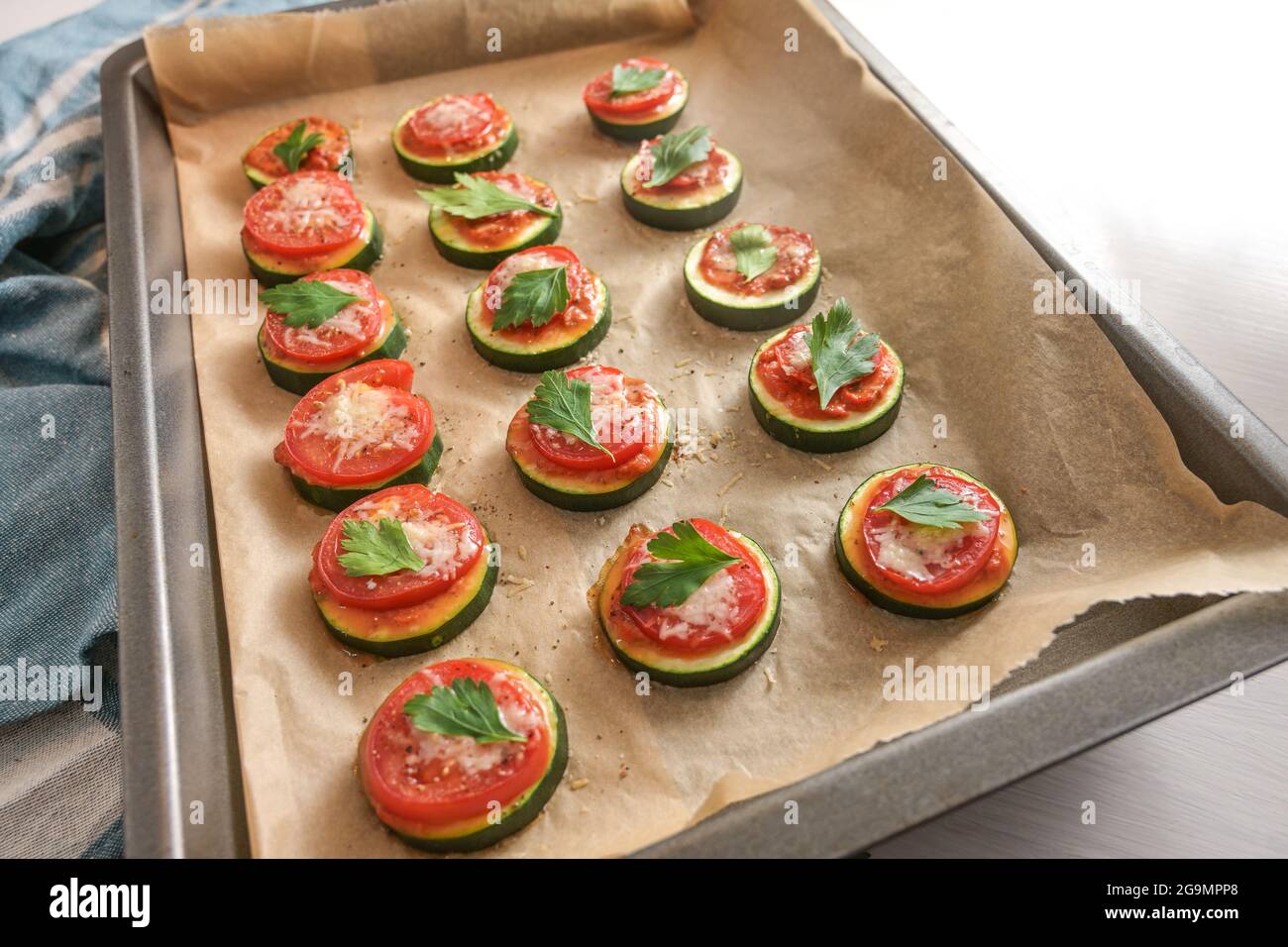 Mini pizza al forno, fatta in casa da fette di zucchine, pomodoro e parmigiano con contorno di prezzemolo su una teglia da forno, focalizzazione selezionata, stretta de Foto Stock