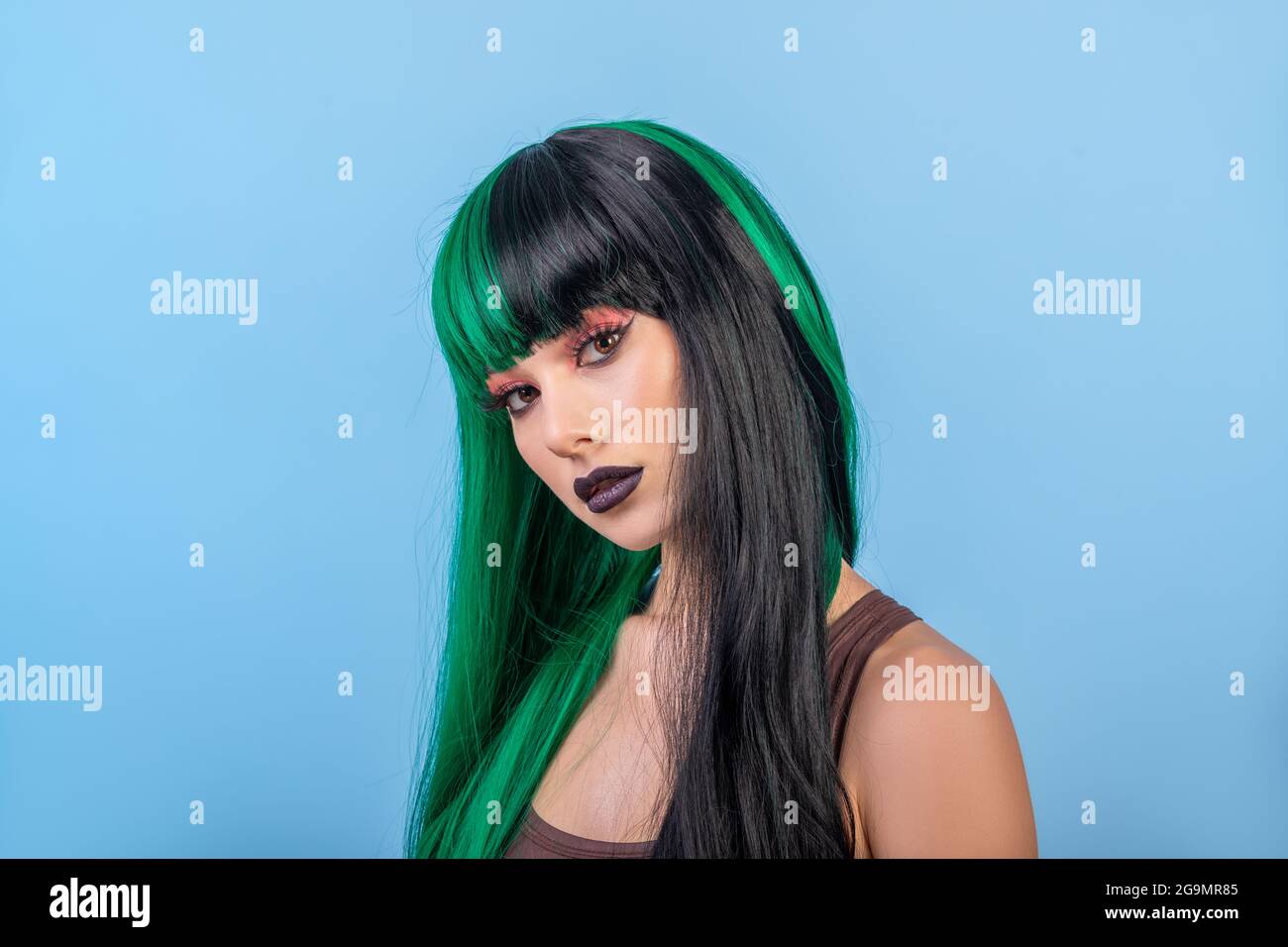 bella donna che indossa colorato verde nero mezzo parrucca su sfondo blu Foto Stock