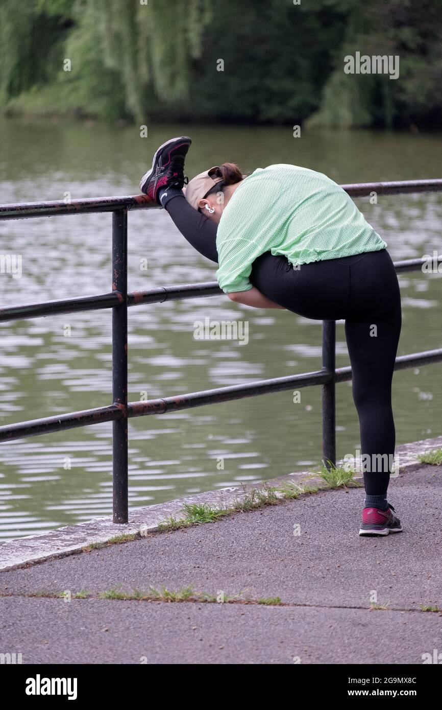Una donna molto flessibile allunga la sua corda su una recinzione vicino al lago in Kissena Park, Flushing, Queens, New York City. Foto Stock