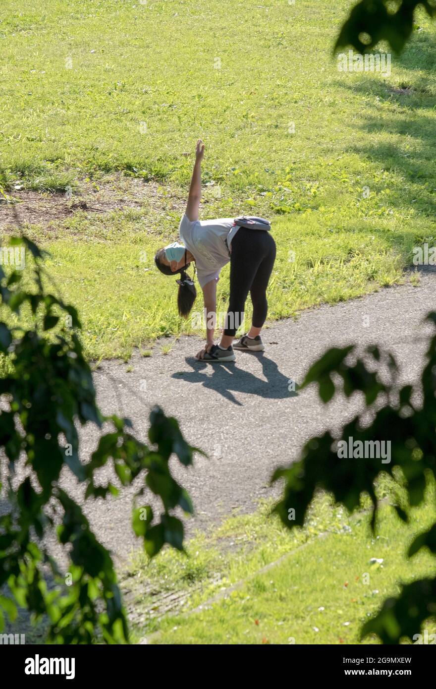 Una donna mascherata non identificata si piega e tocca le dita dei piedi in un parco a Queens, New York City. Foto Stock