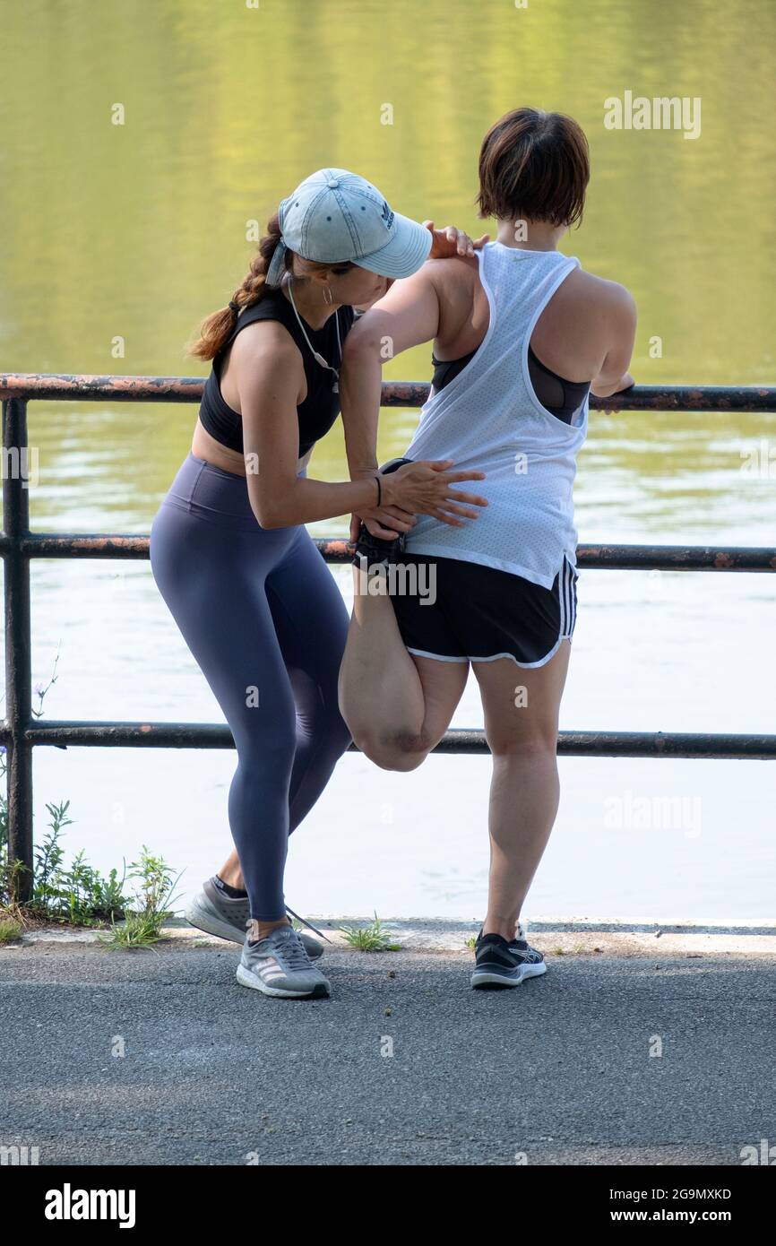 Un personal trainer molto in forma prende un cliente attraverso esercizi di allungamento delle gambe in un parco a Flushing, Queens, New York City. Foto Stock