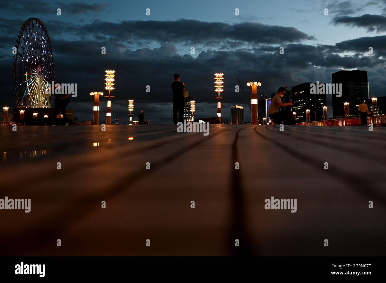 27 luglio 2021, Giappone, Tokio: Passers-by stand su un ponte accanto a una ruota panoramica. Le Olimpiadi di Tokyo 2020 si terranno dal 23.07.2021 al 08.08.2021. Foto: Swen Pförtner/dpa Foto Stock
