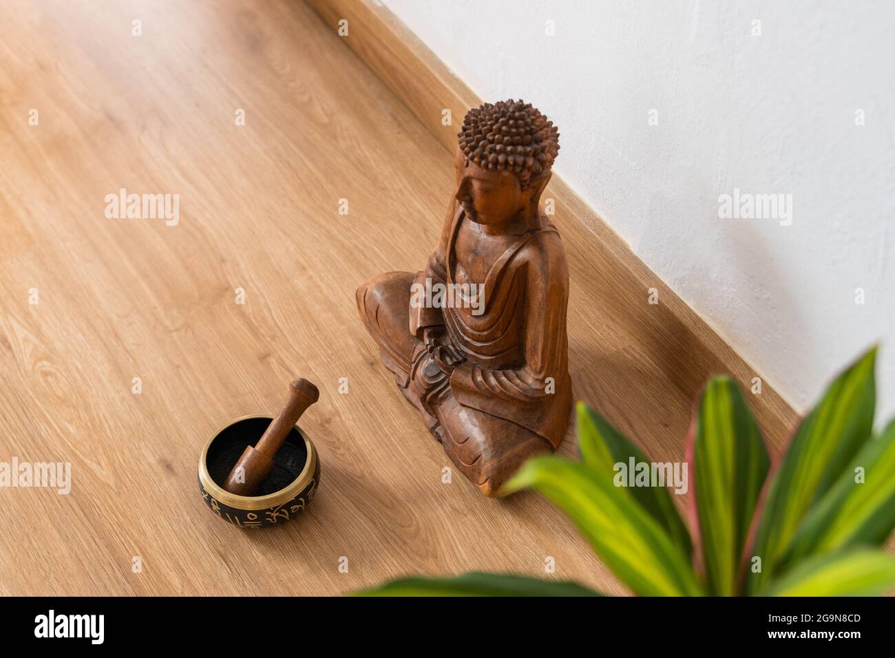 Scultura di buddha in legno accanto a una ciotola tibetana e foglie di pianta su un pavimento in parquet. Foto Stock
