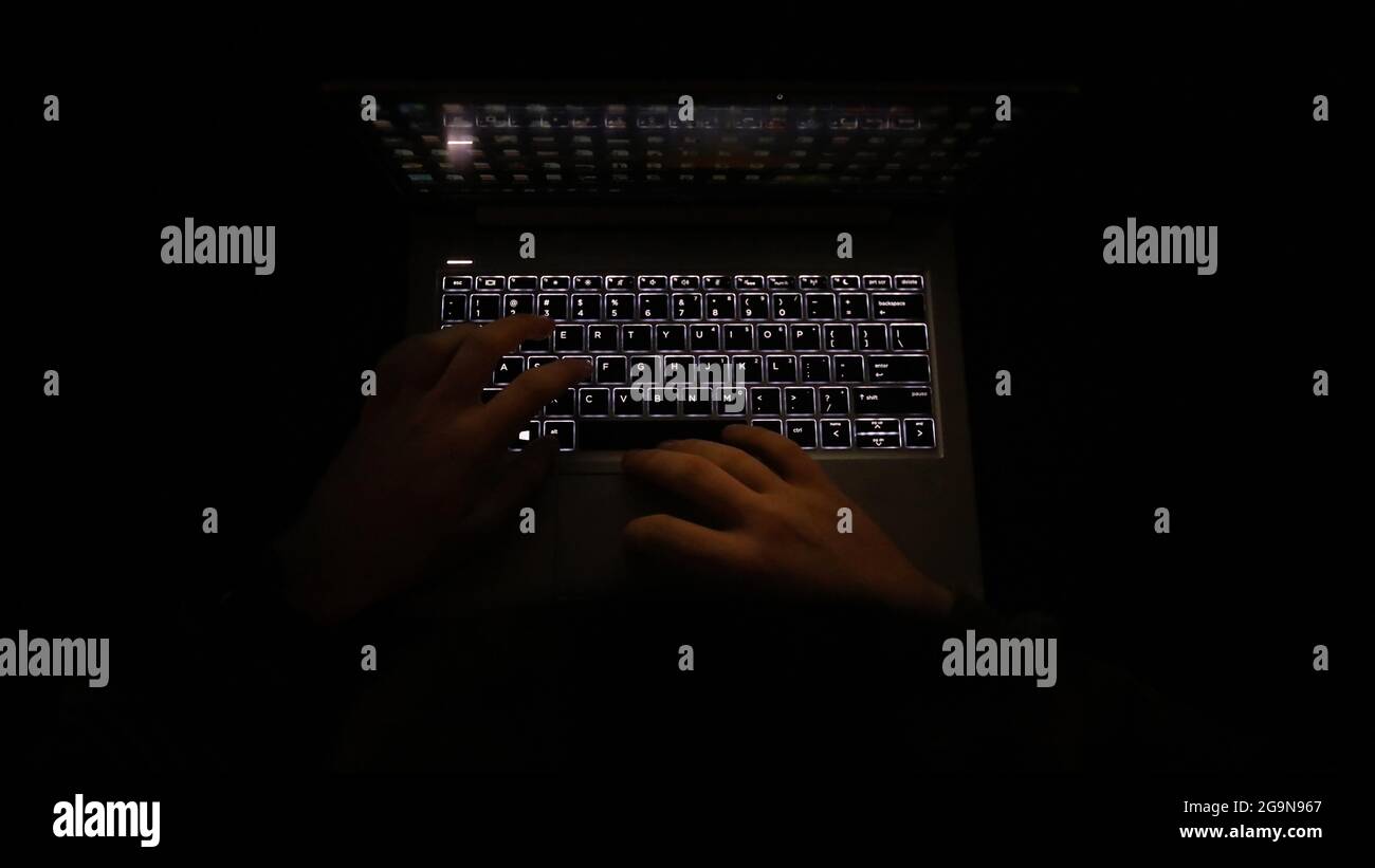Un'immagine notturna semplice e molto scura delle mani su una tastiera illuminata. Utilizzo del computer o del computer portatile al buio. Foto Stock