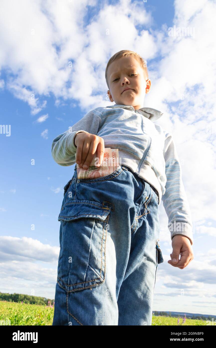 Un bambino di preschooler soddisfatto in jeans ed un maglione tiene i soldi  di carta in