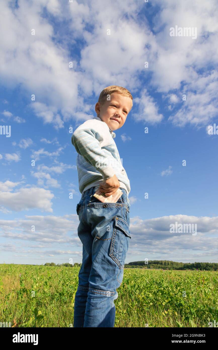 Un bambino di preschooler soddisfatto in jeans ed un maglione tiene i soldi  di carta in