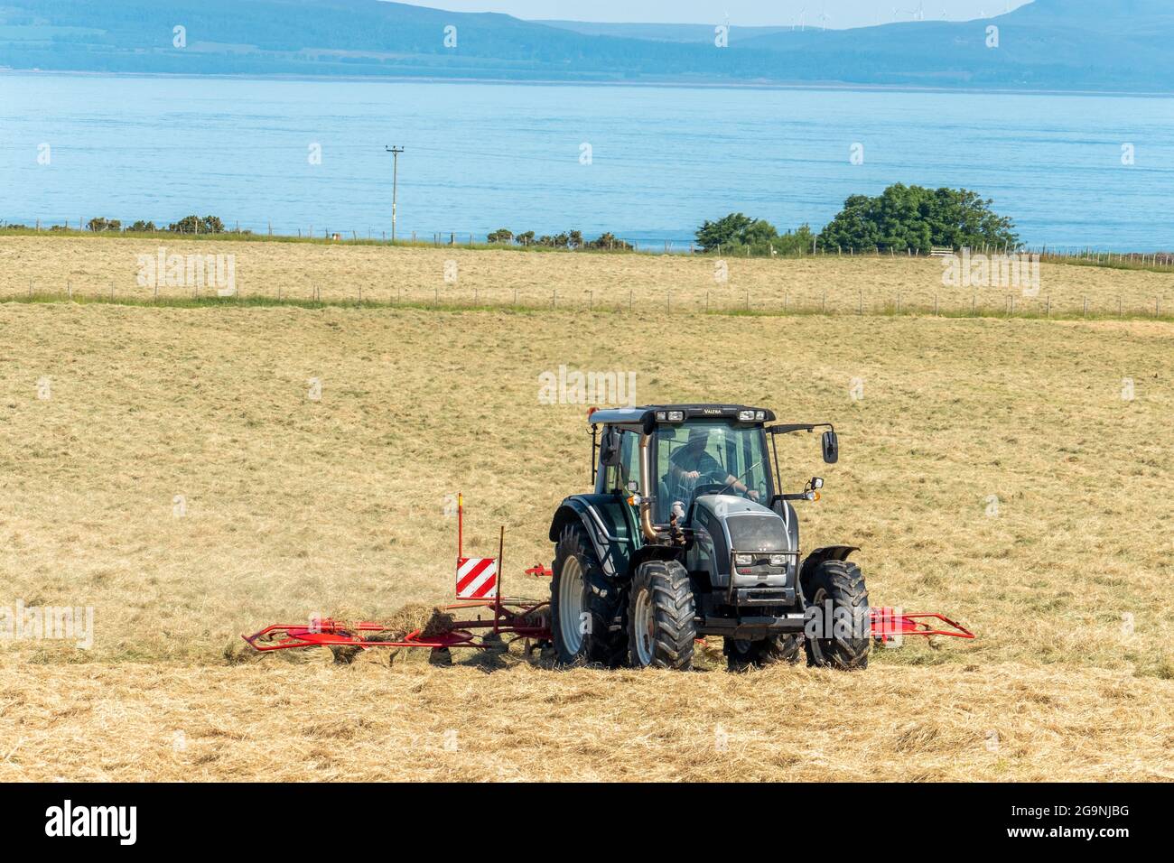 Trattore e macchina haybob che gira fieno vicino a Portmahomack, Pasqua Ross, Scozia. Foto Stock