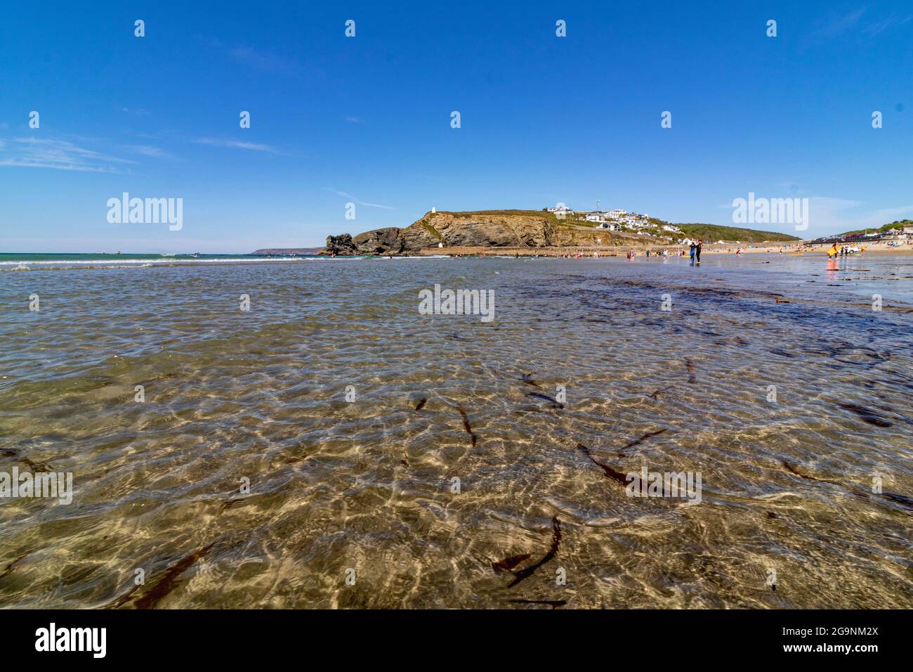 Vista bassa e grandangolare sulle onde dolci, sulla spiaggia, sulla parete del porto distante e sui dettagli della linea costiera all'inizio dell'estate. Spiaggia di Porteath, Cornovaglia. Foto Stock