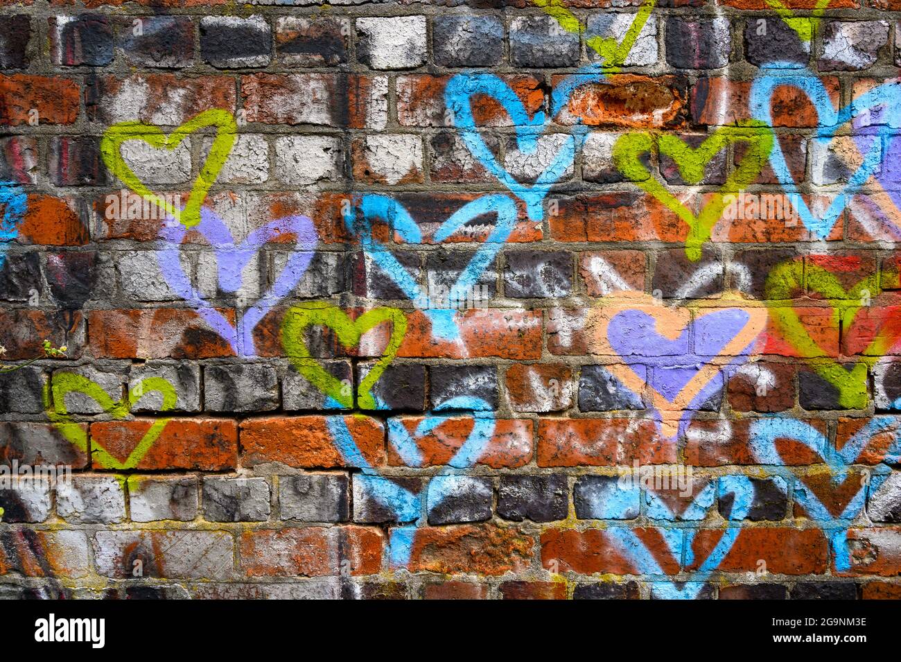 Painted Love: Colorful hearts spray dipinto su un muro di mattoni rossi in difficoltà a Birmingham, Inghilterra, Regno Unito. Foto Stock