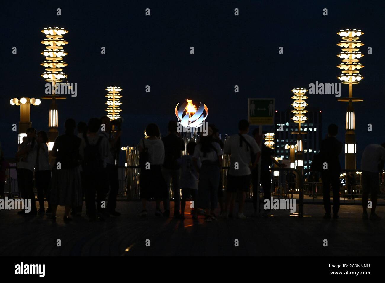Tokio, Giappone. 27 luglio 2021. Passers-by guardare la fiamma olimpica. Le Olimpiadi di Tokyo 2020 si terranno dal 23.07.2021 al 08.08.2021. Credit: Swen Pförtner/dpa/Alamy Live News Foto Stock
