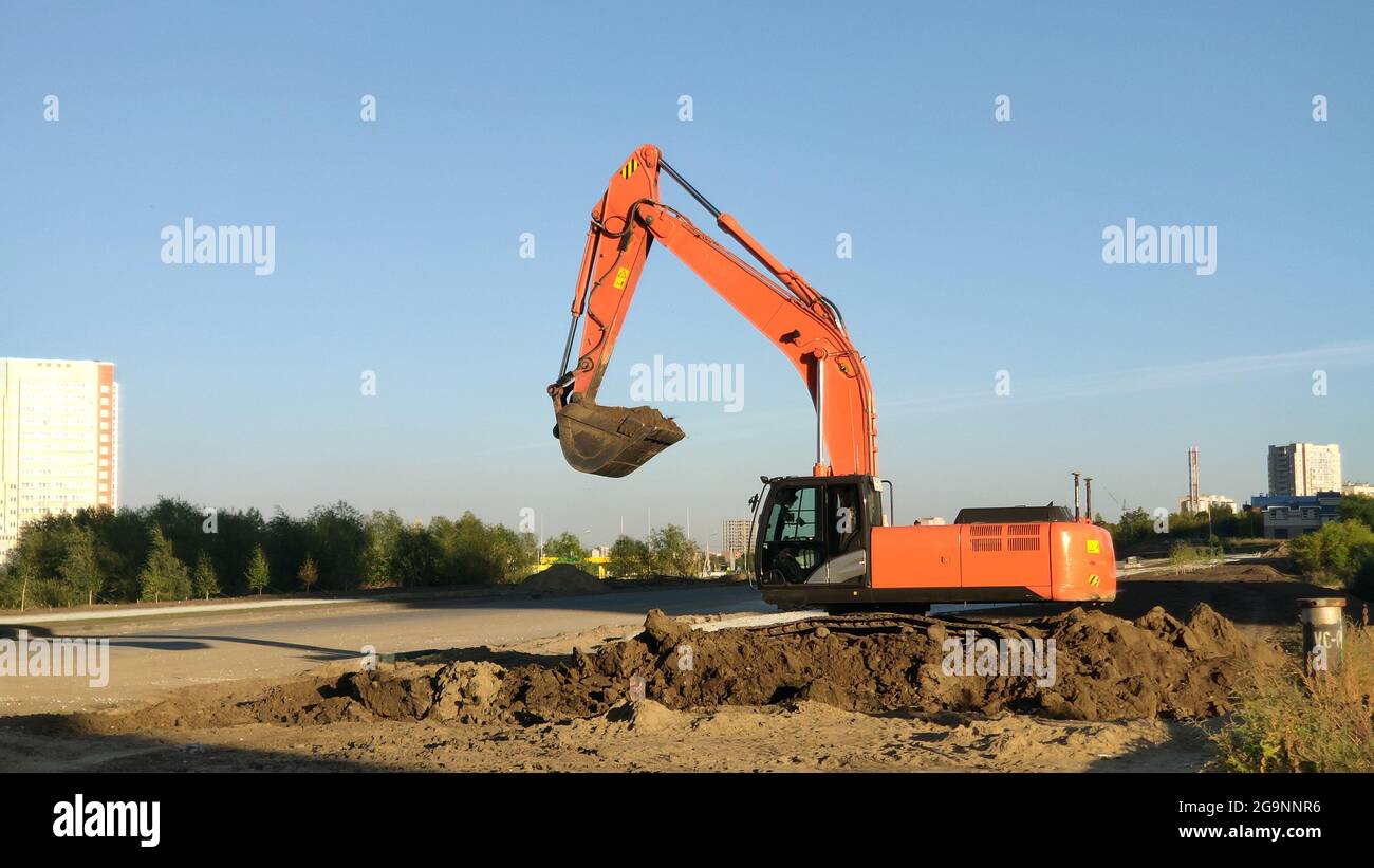 Escavatore giallo durante i lavori di scavo in cantiere. Processo di costruzione di nuove strade o strade urbane Foto Stock