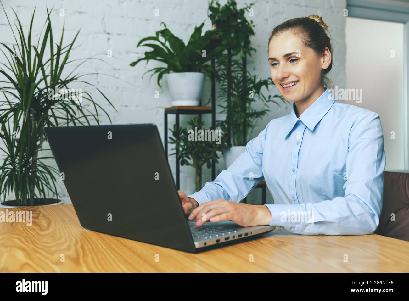 donna sorridente che lavora su un computer portatile in un moderno ufficio luminoso con piante verdi Foto Stock