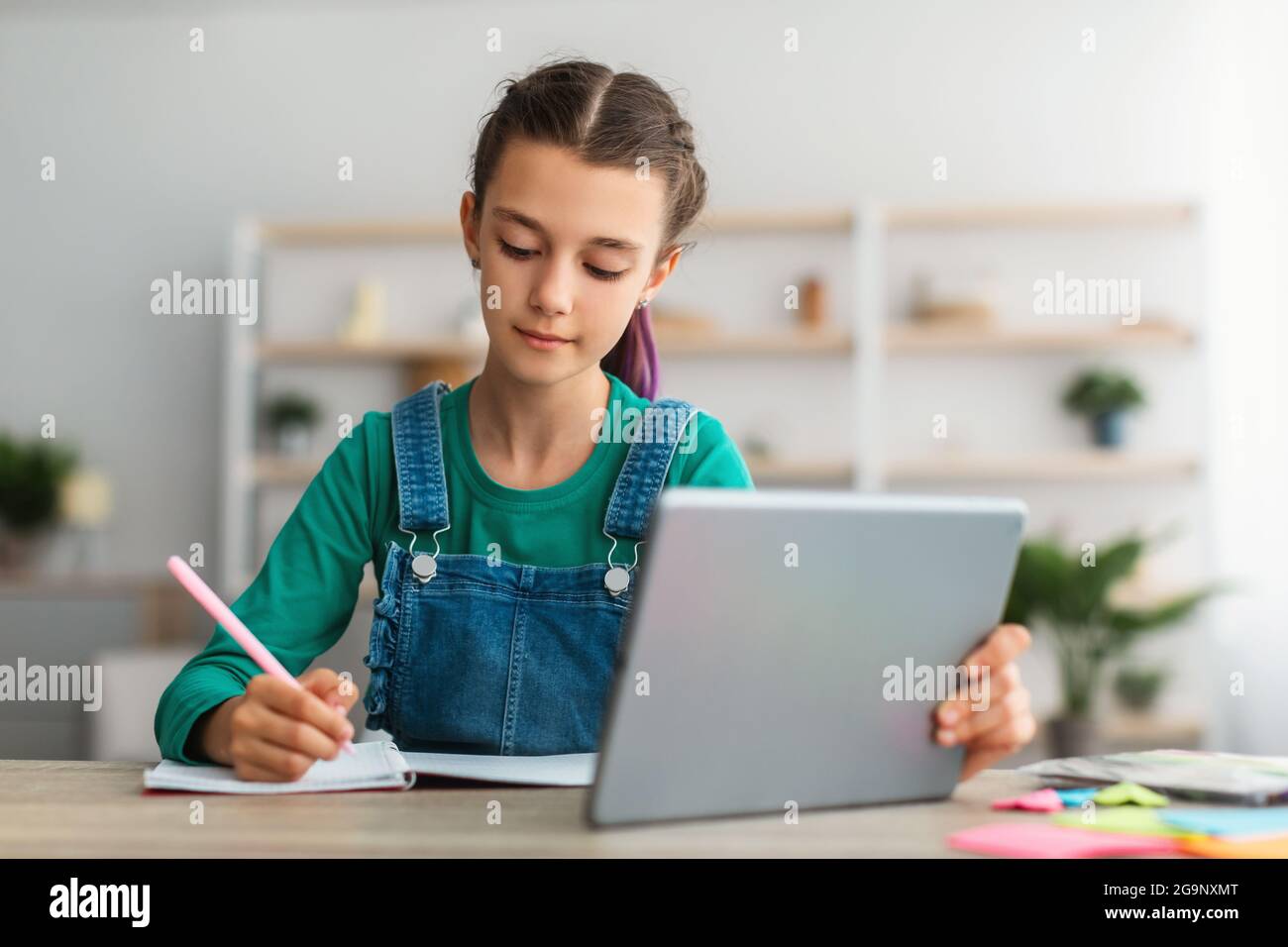 Allievo seduto al tavolo, utilizzando un tablet, scrivendo in un taccuino Foto Stock