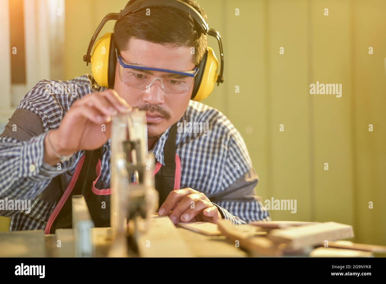 Fuoco selettivo di uomo bello in occhiali e grembiule dentro Officina,Carpentiere in funzione Foto Stock