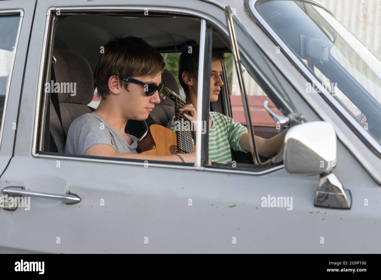 Due giovani in macchina. Il ragazzo suona la chitarra in macchina. Compagnia allegra di giovani. Viaggia insieme. Divertimento passatempo. Foto Stock