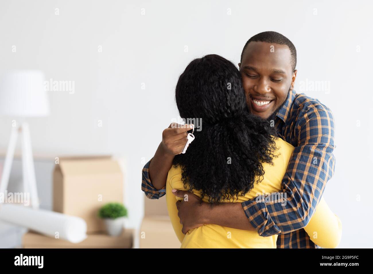 Happy Black Man Holding Home Keys, abbracciando la moglie dopo l'acquisto di un nuovo appartamento Foto Stock