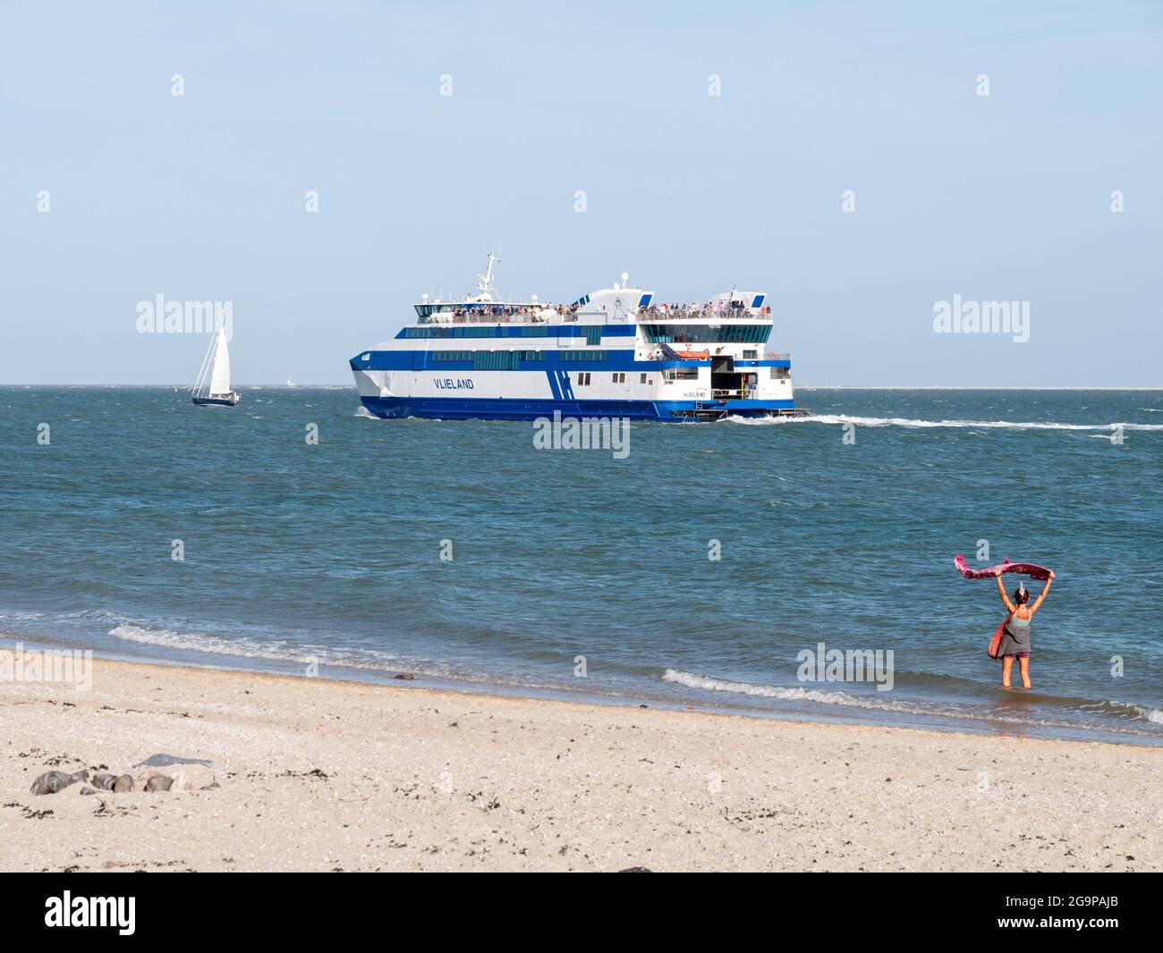 Donna che sventolava Arrivederci ai passeggeri in traghetto che lasciano il porto dell'isola della Frisia occidentale Vlieland attraversando Waddensea a Harlingen, Paesi Bassi Foto Stock