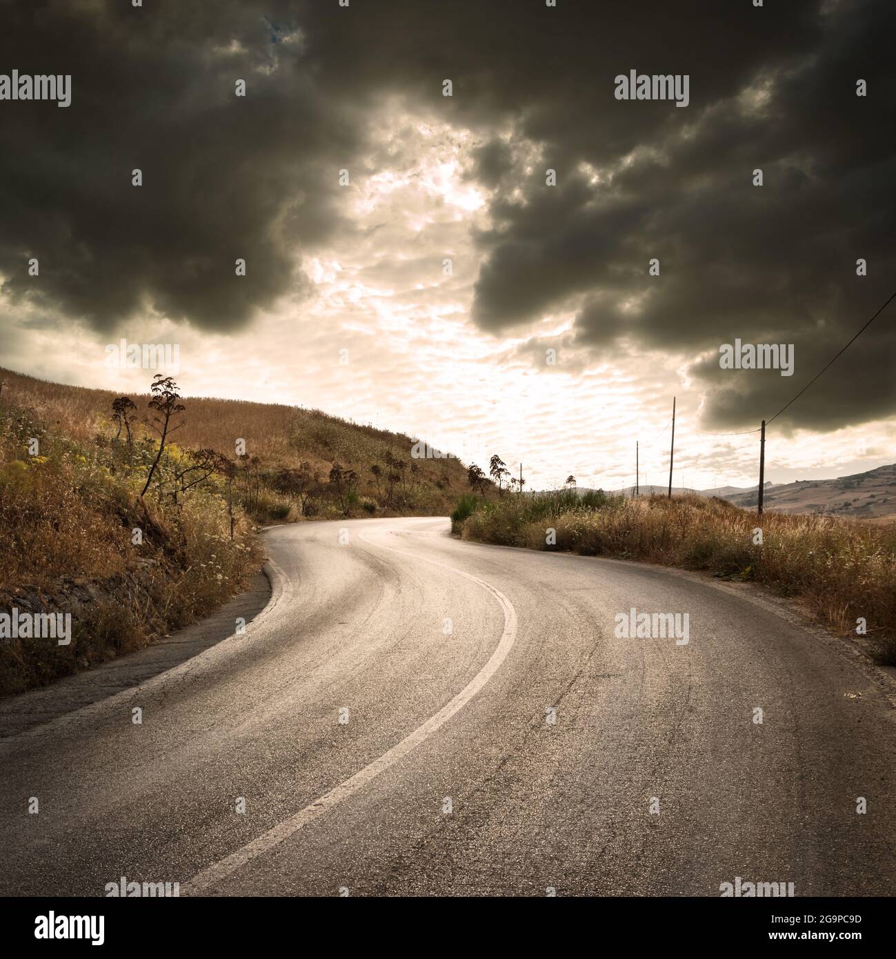 strada tortuosa di campagna sotto le nuvole tempestose al tramonto Foto Stock