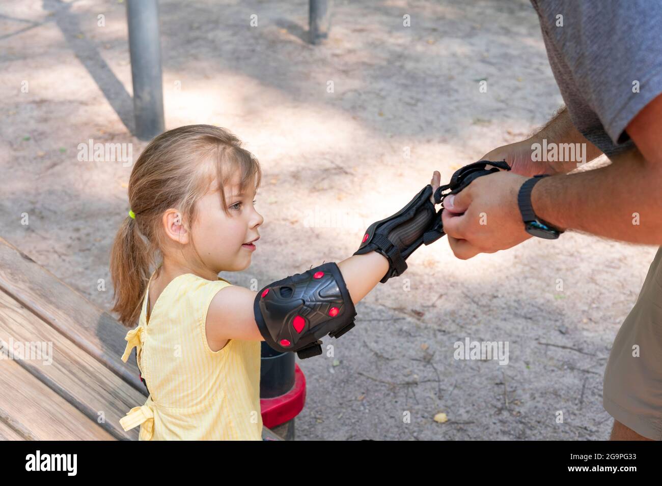 Padre papà che mette in bicicletta sulla figlia le ginocchiere e le ginocchiere di protezione. Aiuto e cura per i bambini. Sicurezza in città su scooter o bicicletta Foto Stock