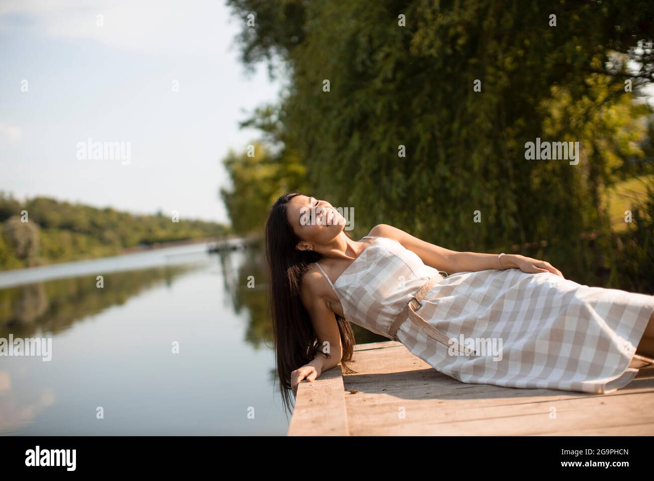 rilassante giovane donna sul molo di legno al lago calmo Foto Stock