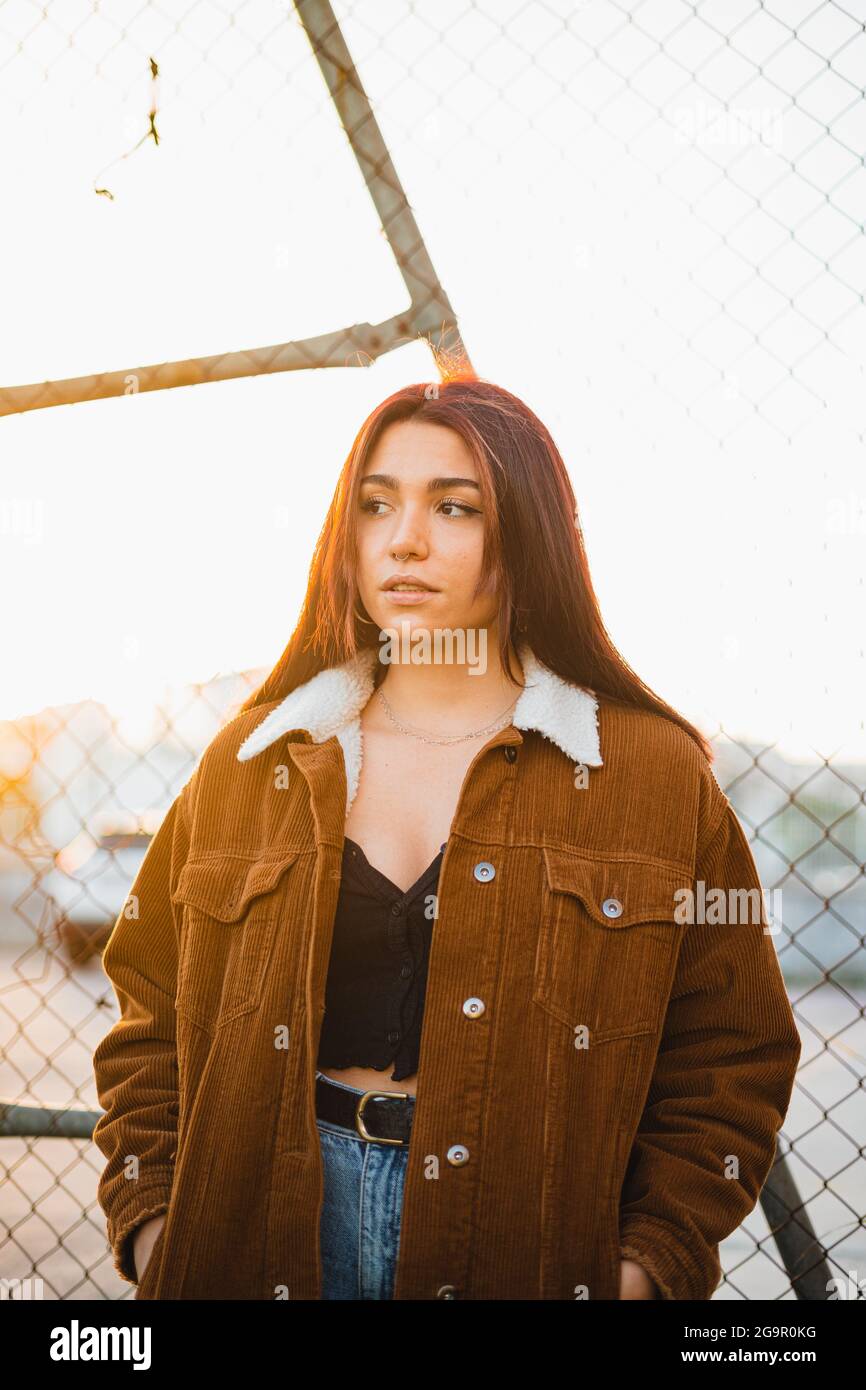 Ritratto di bella ragazza adolescente in piedi contro catena-link recinto  durante il tramonto. Indossa una giacca marrone e jeans blu Foto stock -  Alamy