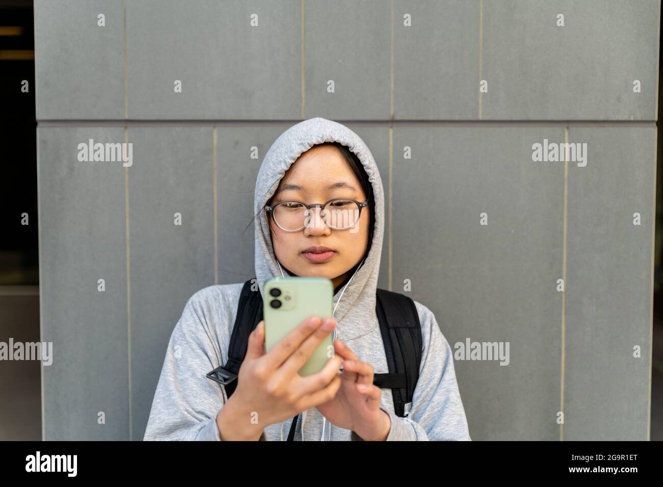 Giovane adulto asiatico usando il telefono delle cellule che indossa gli occhiali Foto Stock