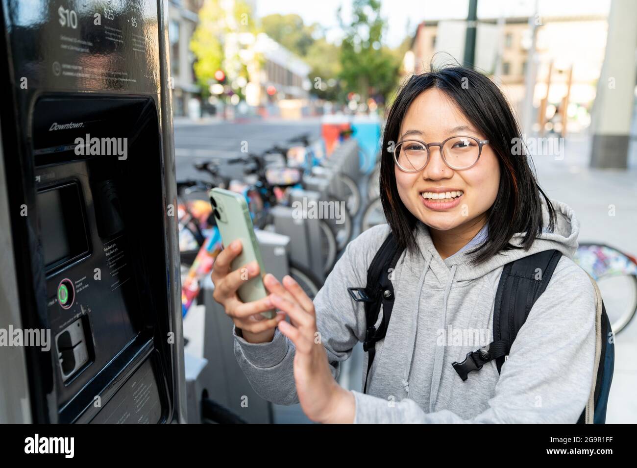 Giovane donna che usa lo smartphone presso la stazione di noleggio biciclette Foto Stock