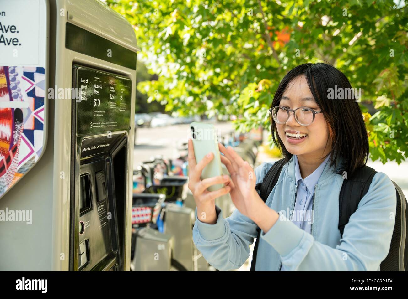 Giovane donna che utilizza il telefono cellulare alla stazione di condivisione della bicicletta mentre si è in viaggio Foto Stock