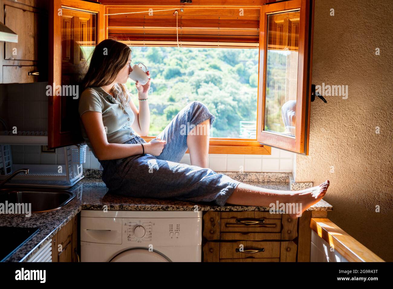 Adolescente donna seduta guardando fuori la finestra bere caffè. Foto Stock