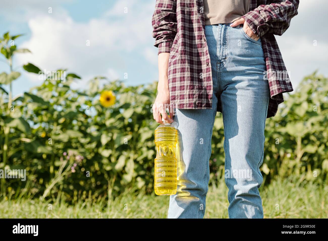 Matura allegra agricoltore femminile in beanie e abbigliamento da lavoro guardando sei sorridente mentre ti trovi di fronte alla fotocamera campo verde e cielo Foto Stock