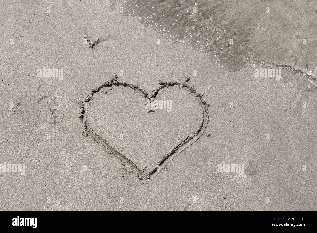 Disegno a mano della forma del cuore e dell'onda del mare nella sabbia sulla spiaggia. Concetto di amore estivo. Primo piano, spazio di copia per la progettazione Foto Stock