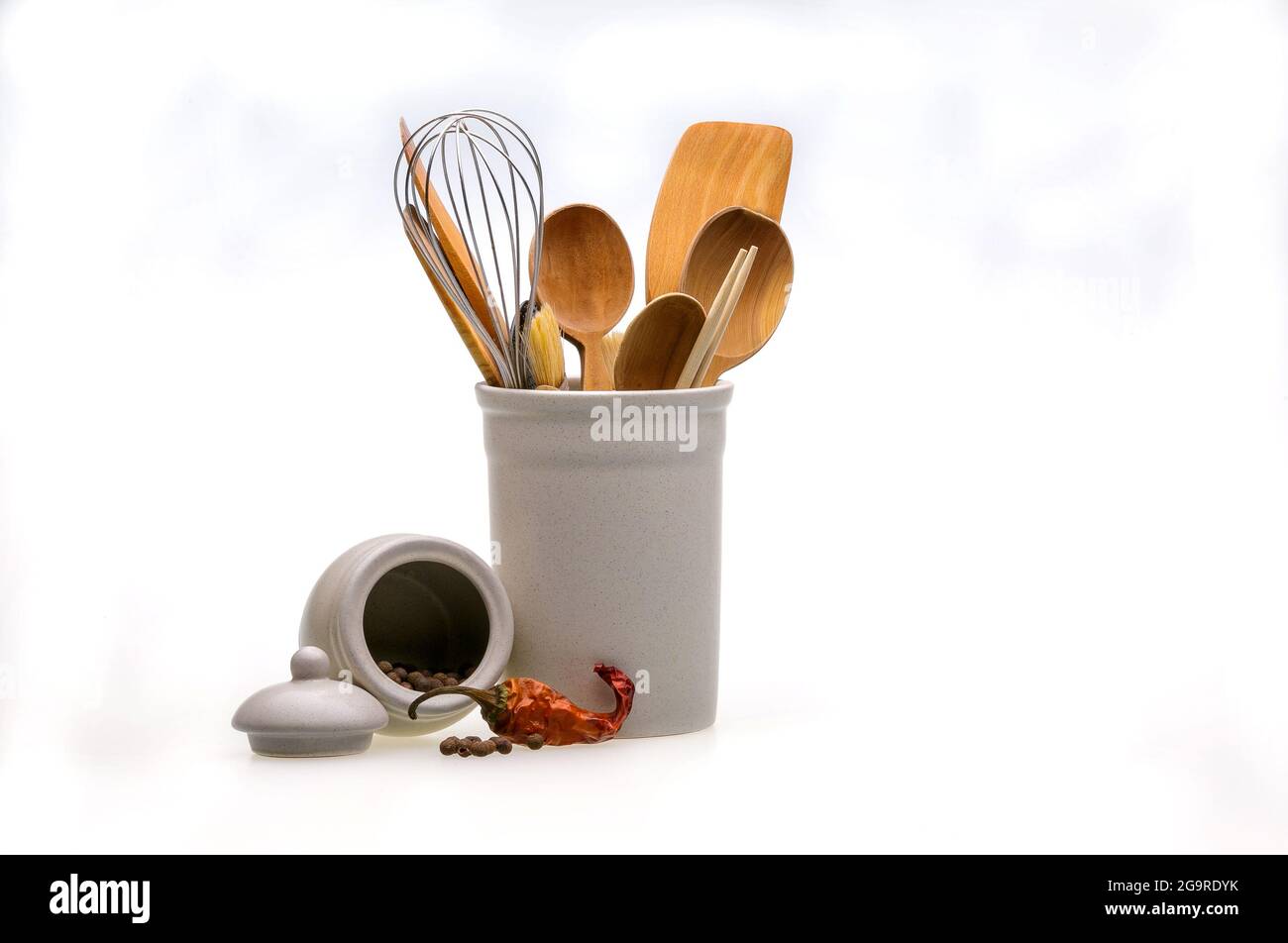 Utensili in legno per cucinare in un bicchiere bianco e pepe rosso caldo. Cucchiai da cucina, sessole, forcelle isolate su sfondo bianco. In stile scandinavo Foto Stock