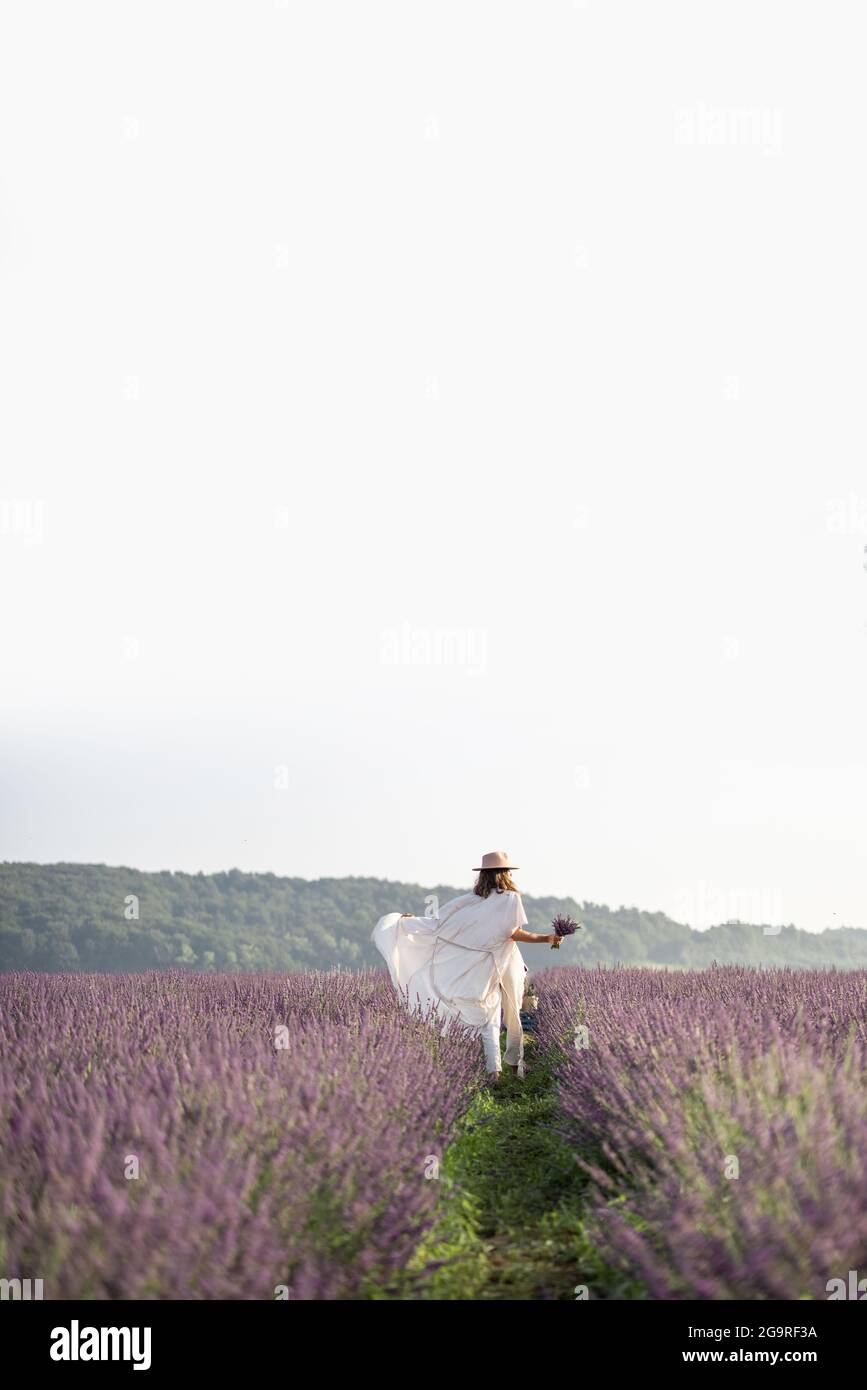 Giovane donna che corre sul campo di lavanda con bouquet di fiori violetti e godere della bellezza e del profumo della natura. Calma e concetto di consapevolezza. Spazio di copia Foto Stock