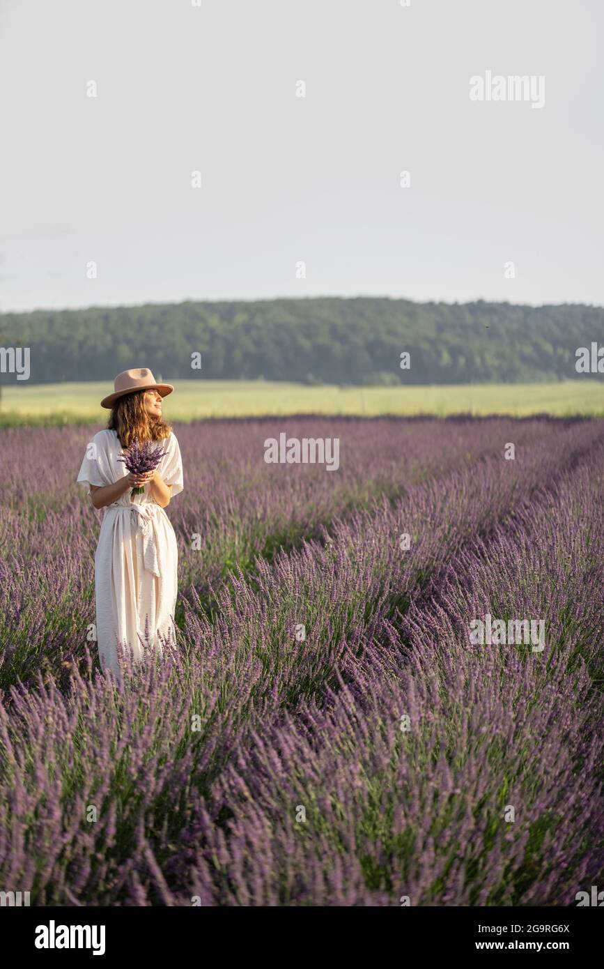 Giovane donna che si trova sul campo di lavanda fiorito con bouquet di fiori viola e godere della bellezza della natura. Calma e concetto di consapevolezza. Spazio di copia Foto Stock