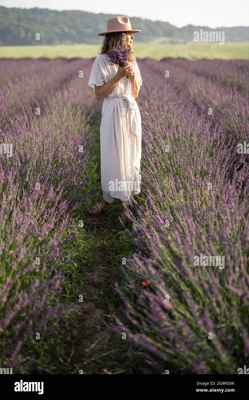 Giovane donna che si trova sul campo di lavanda con bouquet di fiori viola e godere della bellezza della natura. Calma e concetto di consapevolezza. Foto Stock